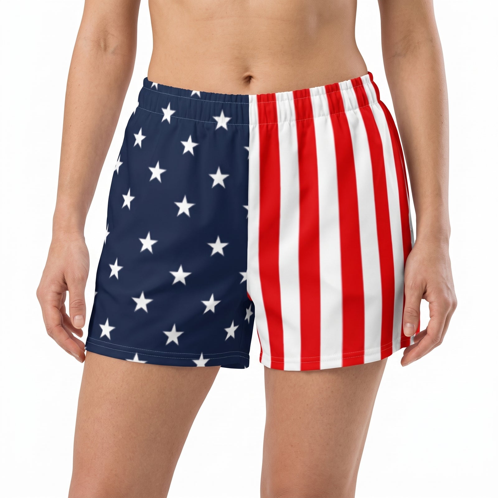 A person wearing swim trunks with a split American flag design, featuring white stars on a navy blue left side and red and white vertical stripes on the right, against a plain white background.