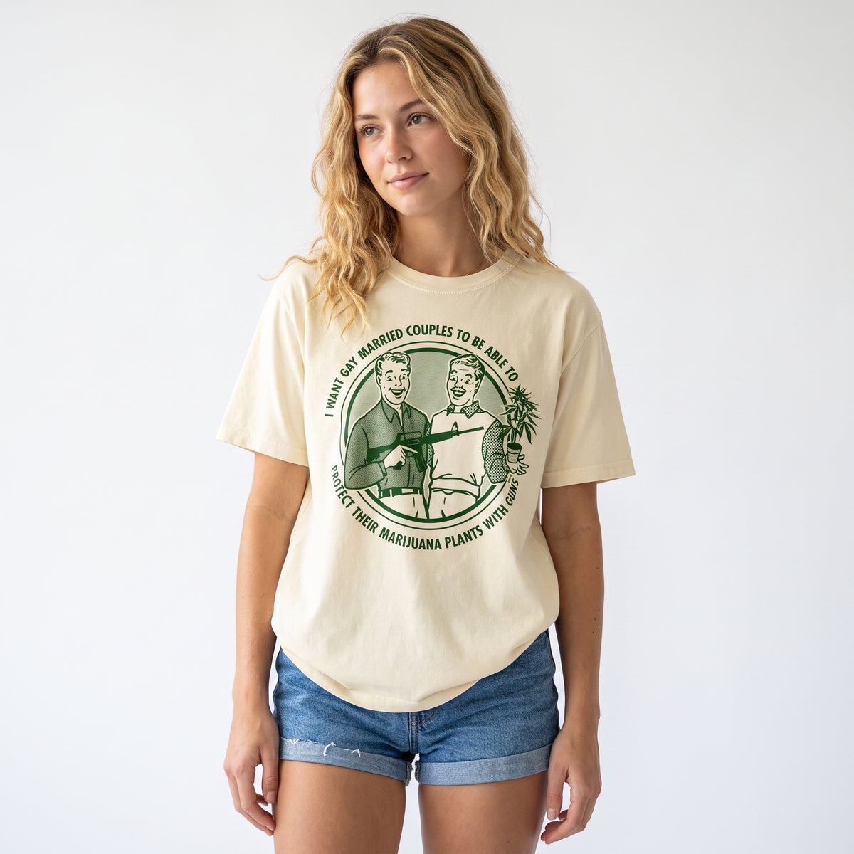 A woman modeling a cream-colored graphic t-shirt with a green vintage-style print on the front, paired with denim shorts, against a plain white background.