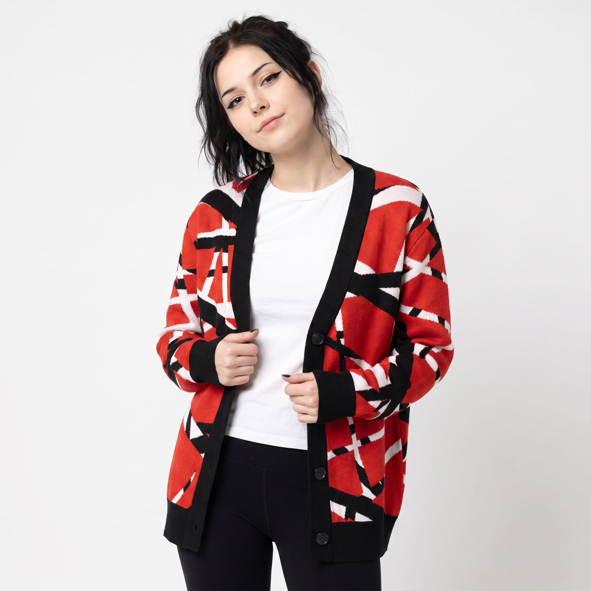 A woman modeling a red open-front cardigan with a black and white geometric pattern, worn over a white t-shirt and black pants against a light gray background.