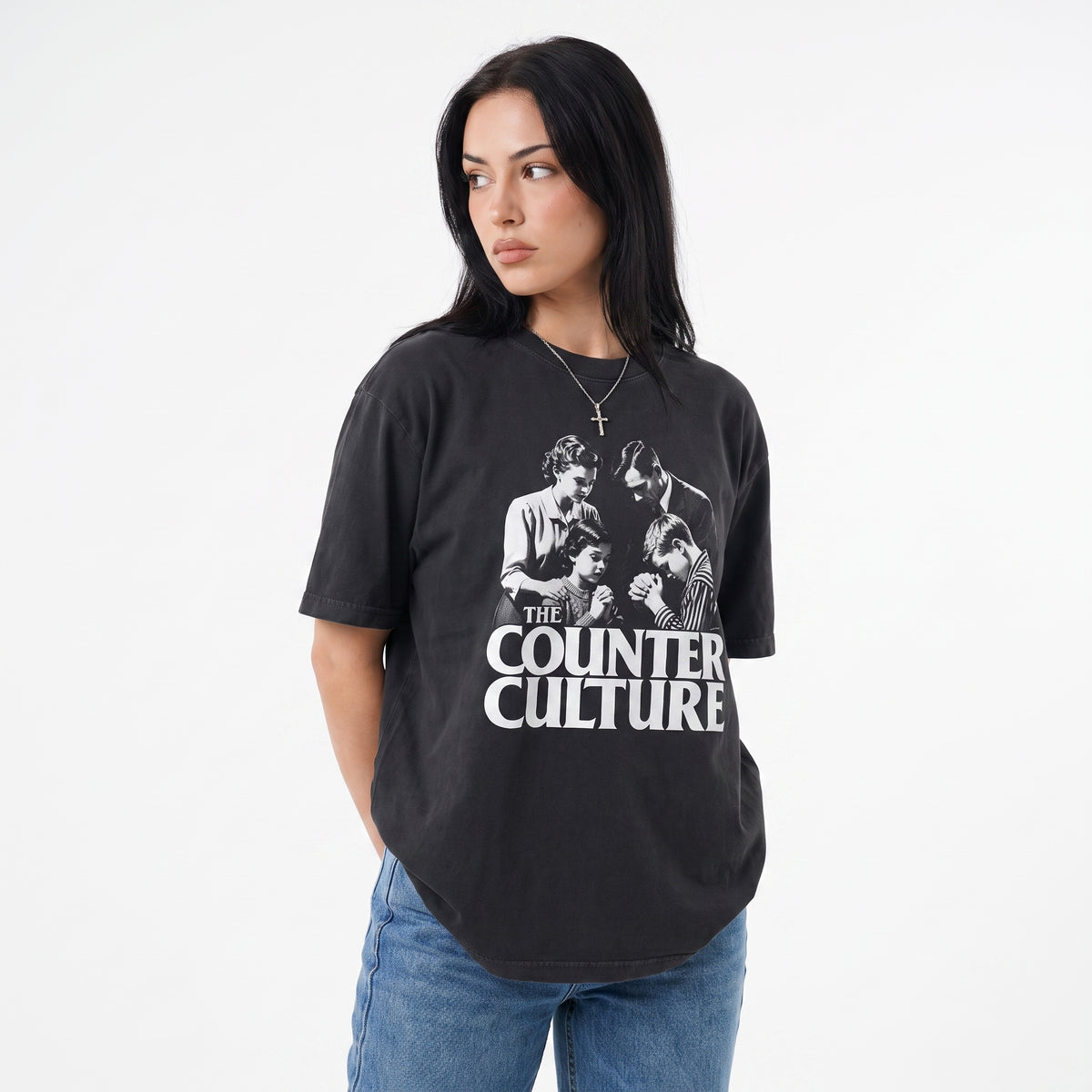 A woman wearing a black graphic t-shirt with a white print of the band 'The Counter Culture' and blue jeans, photographed against a plain white background.