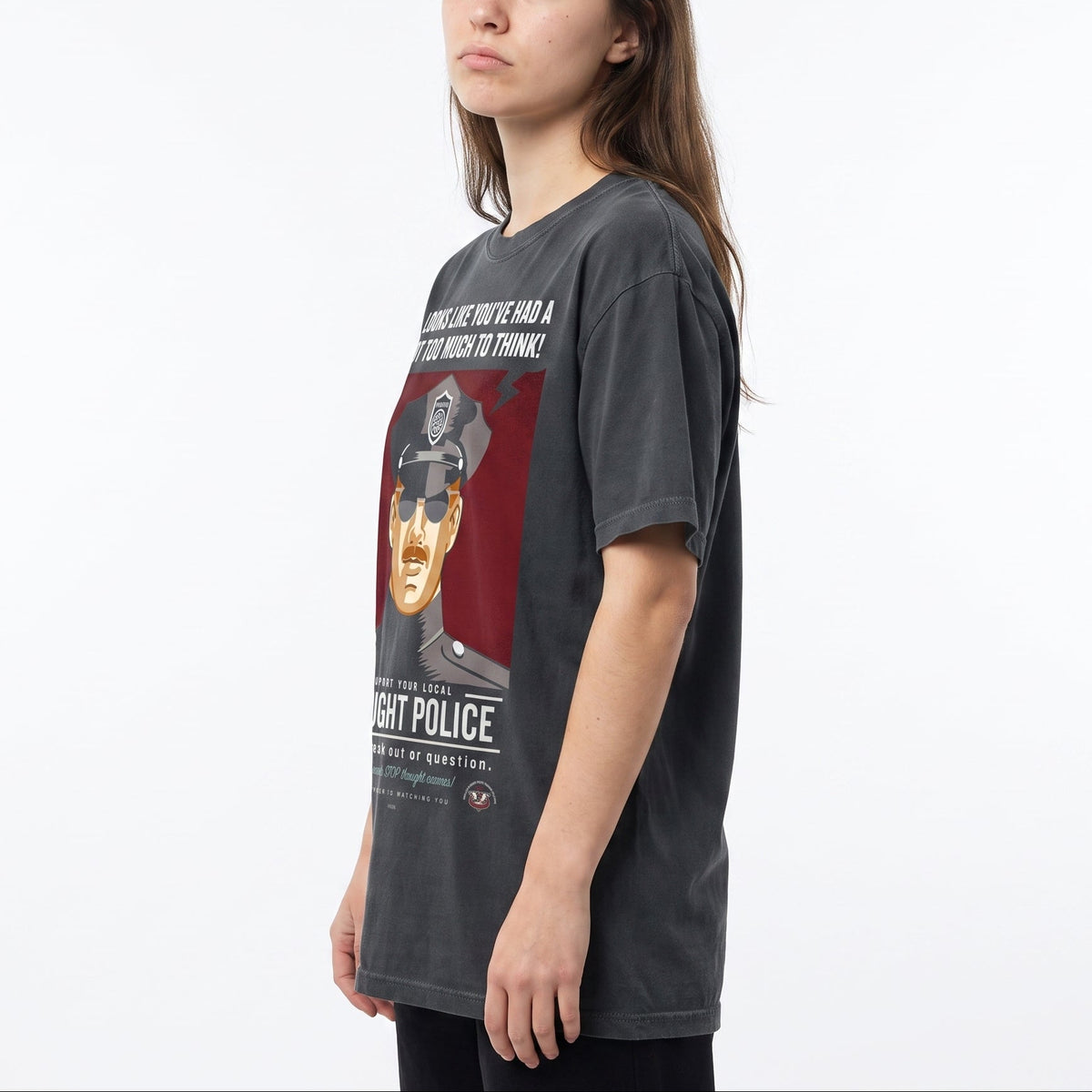 A woman wearing a dark gray graphic t-shirt with a red and black print featuring a Liberty Maniacs Thought Police t-shirt that says, 'It look slike you've had too much to think."