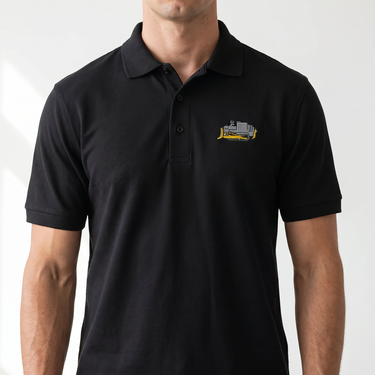 A man wearing a black short-sleeve polo shirt with a small embroidered killdozer on the left chest, shown against a plain light background.