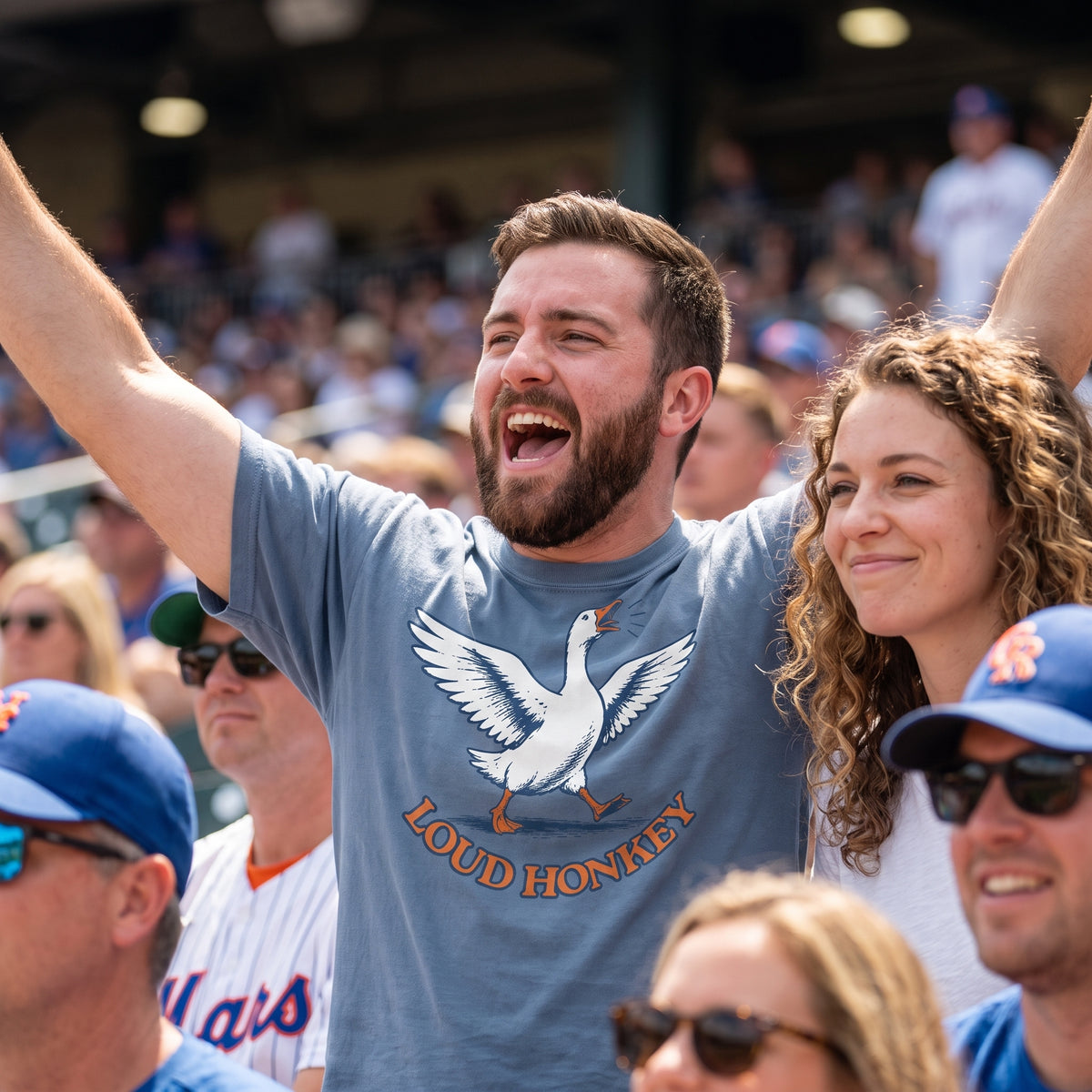 Man cheering at a baseball game wearing a Loud Honkey garment-dyed t-shirt with a honking goose graphic, Blue Jean color