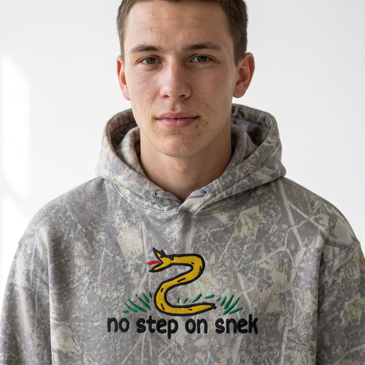 Man wearing Forest Camo No Step on Snek embroidered hoodie, front studio view