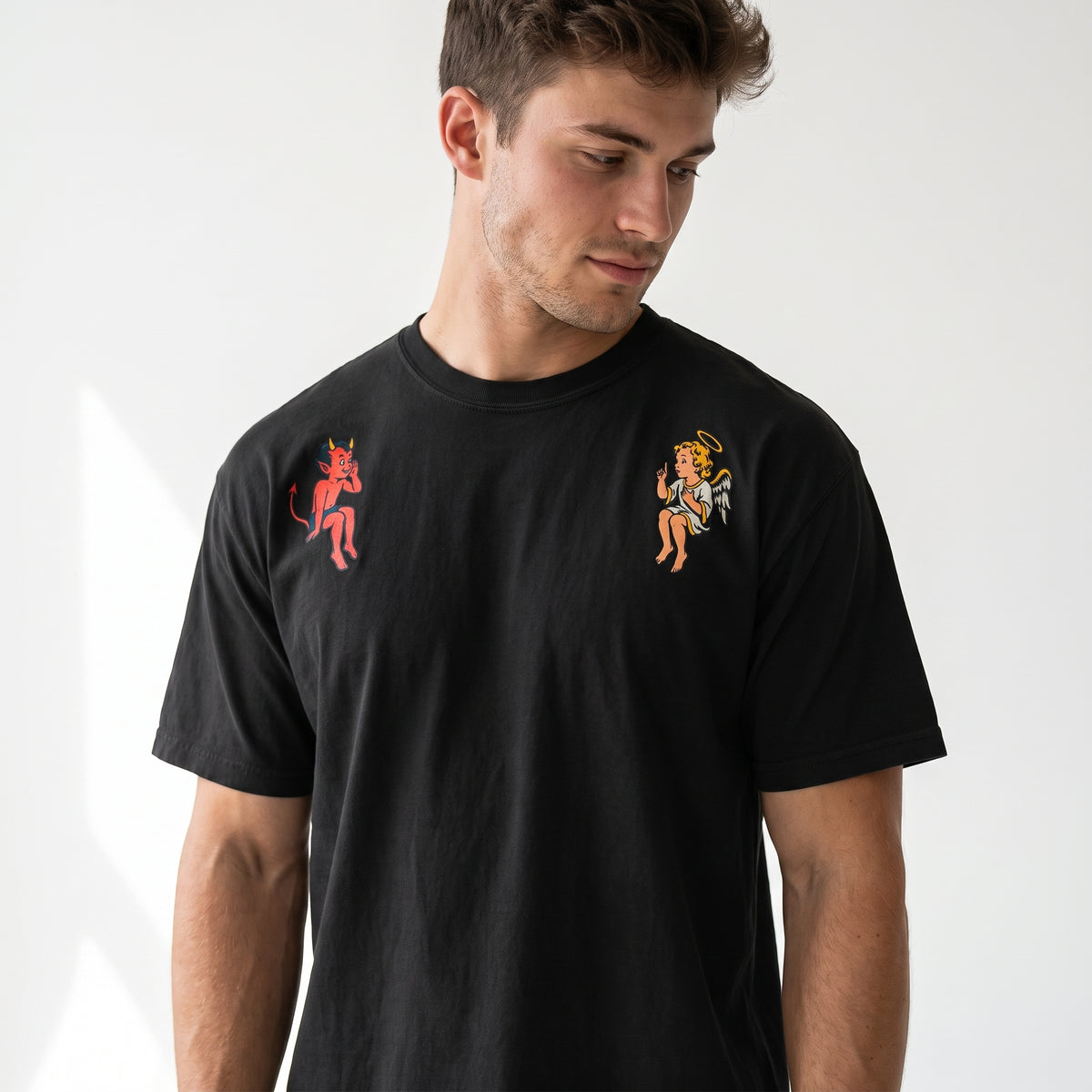 Male model looking at the angel and devil graphics on a black shoulder tee