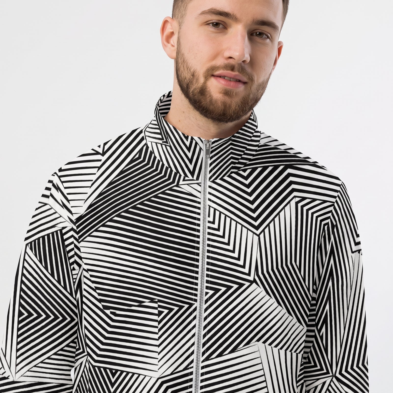 A man wearing a black and white dazzle naval camo geometric patterned zip-up jacket against a light gray background.