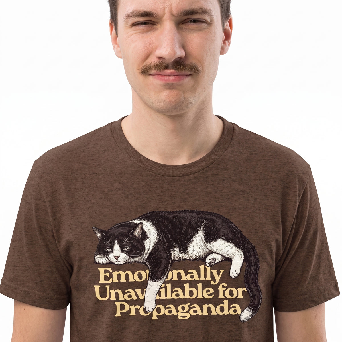 A man wearing a brown heathered t-shirt with a graphic of a black and white cat lying down above the text 'Emotionally Unavailable for Propaganda' in beige.