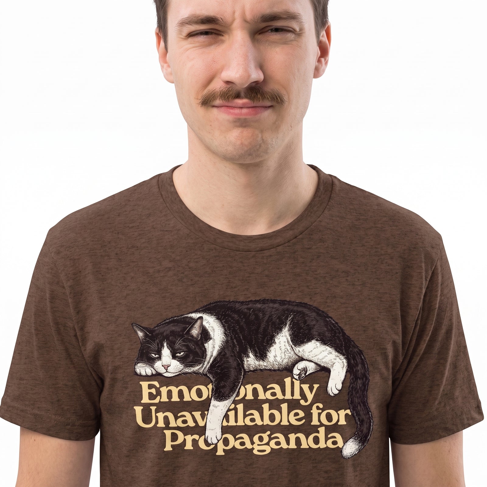 A man wearing a brown heathered t-shirt with a graphic of a black and white cat lying down above the text 'Emotionally Unavailable for Propaganda' in beige.