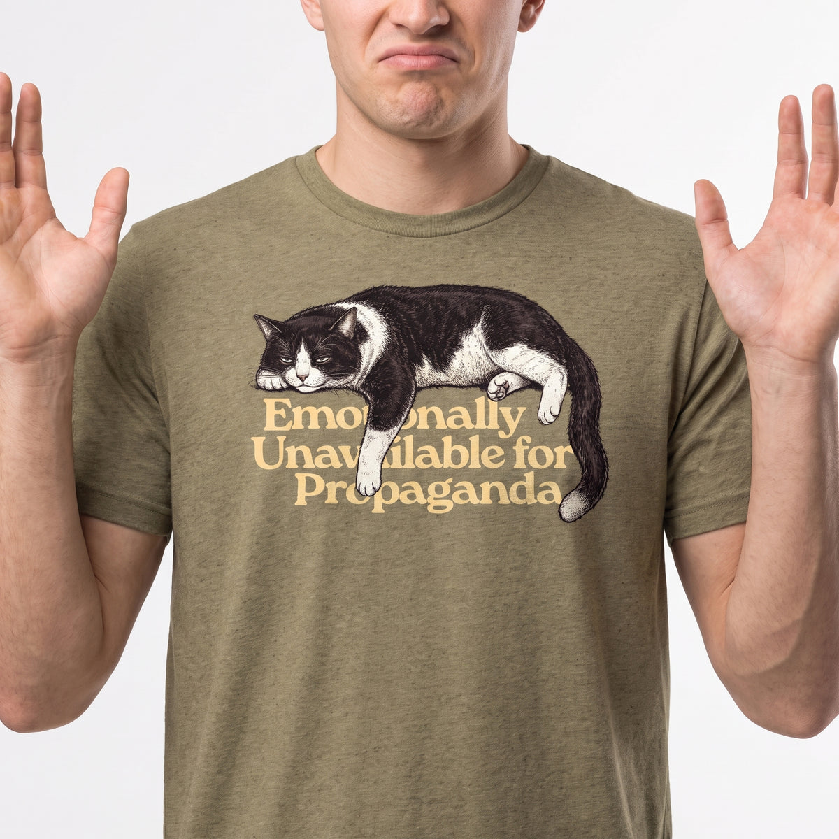 A man wearing an olive green t-shirt with a graphic of a sleeping black and white cat and the text 'Emotionally Unavailable for Propaganda'.