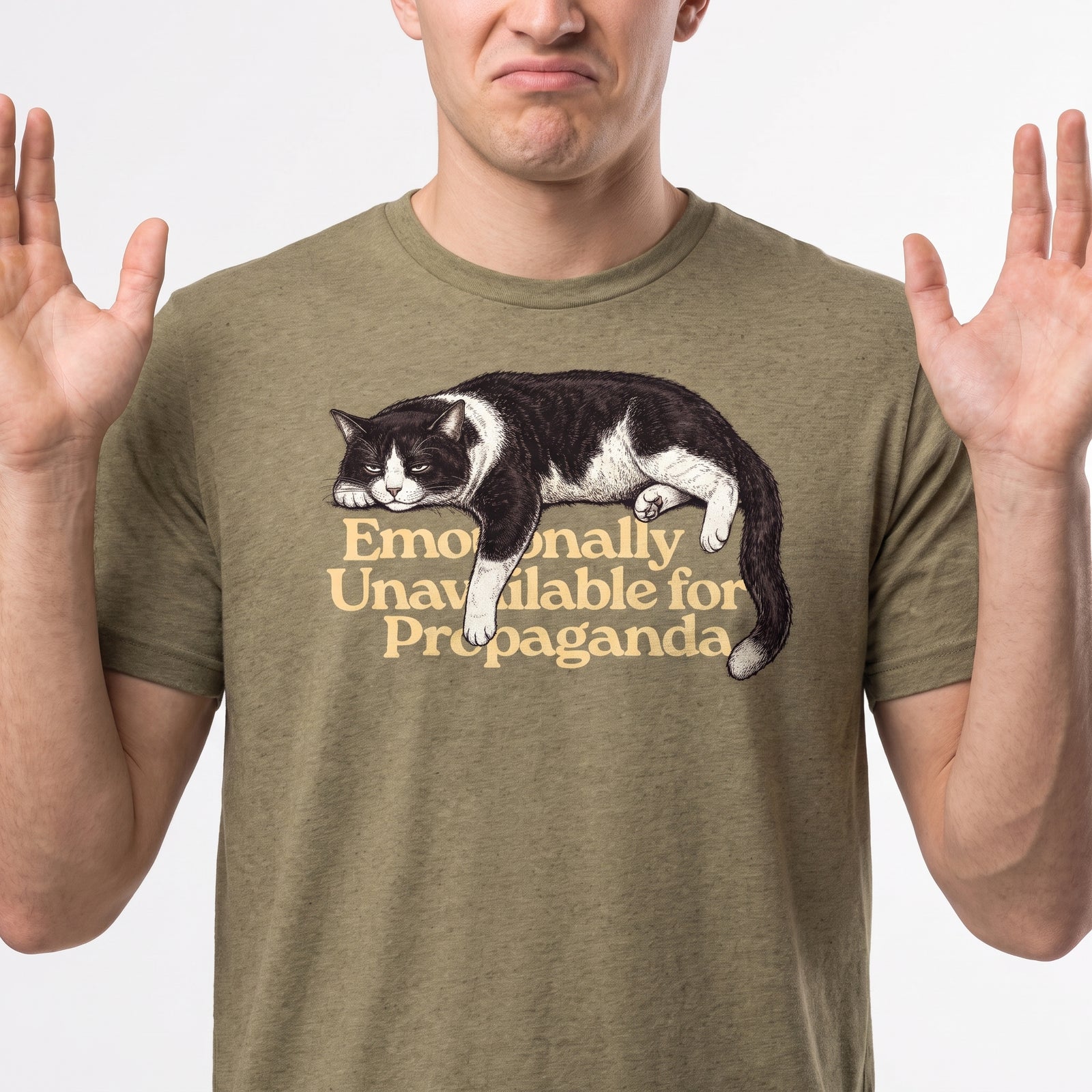 A man wearing an olive green t-shirt with a graphic of a sleeping black and white cat and the text 'Emotionally Unavailable for Propaganda'.
