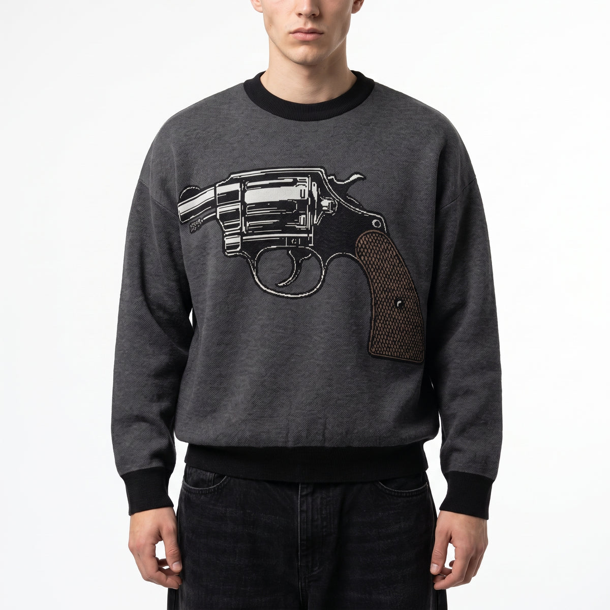 A man wearing a dark gray crewneck Jacquard-knit sweater from Liberty Maniacs with a large black and silver revolver graphic on the front, paired with dark jeans, against a plain white background.