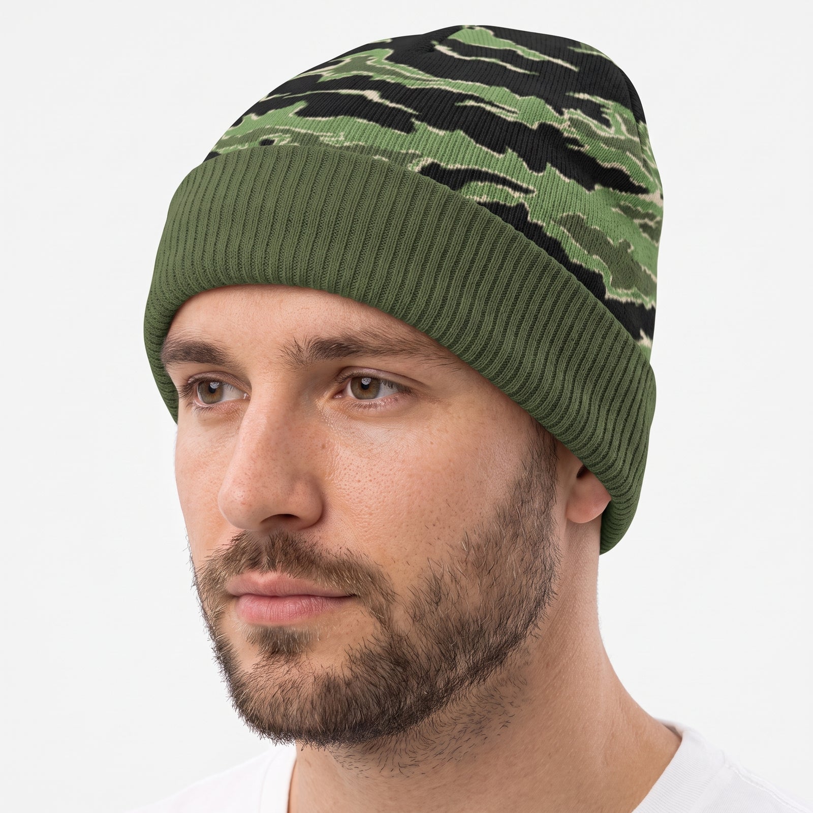 A man wearing a green and black tiger-stripe camouflage knit beanie hat, shown in a close-up profile against a light gray background.