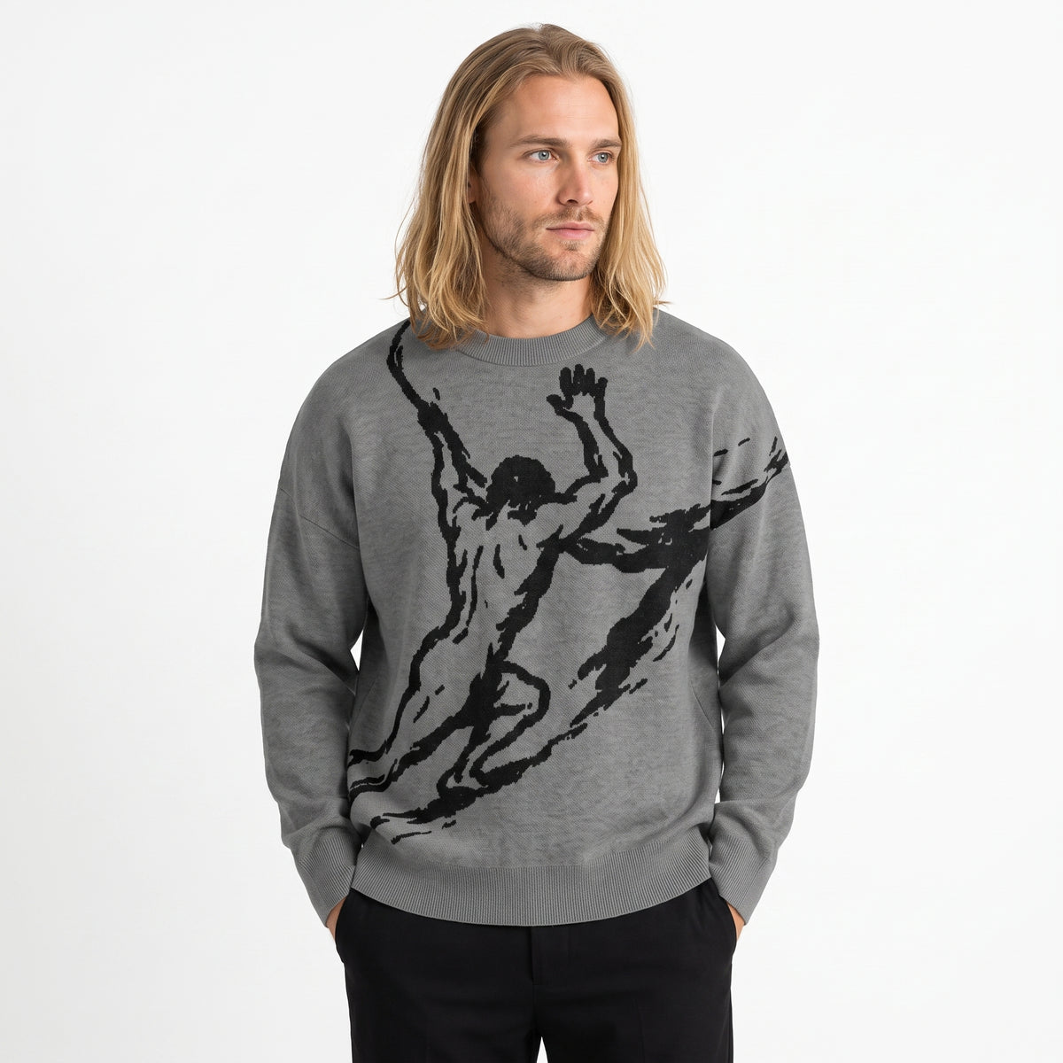 A man with long blonde hair wearing a heather gray crewneck sweater with a large black graphic of a muscular Sisyphus, paired with black pants, against a plain white background.