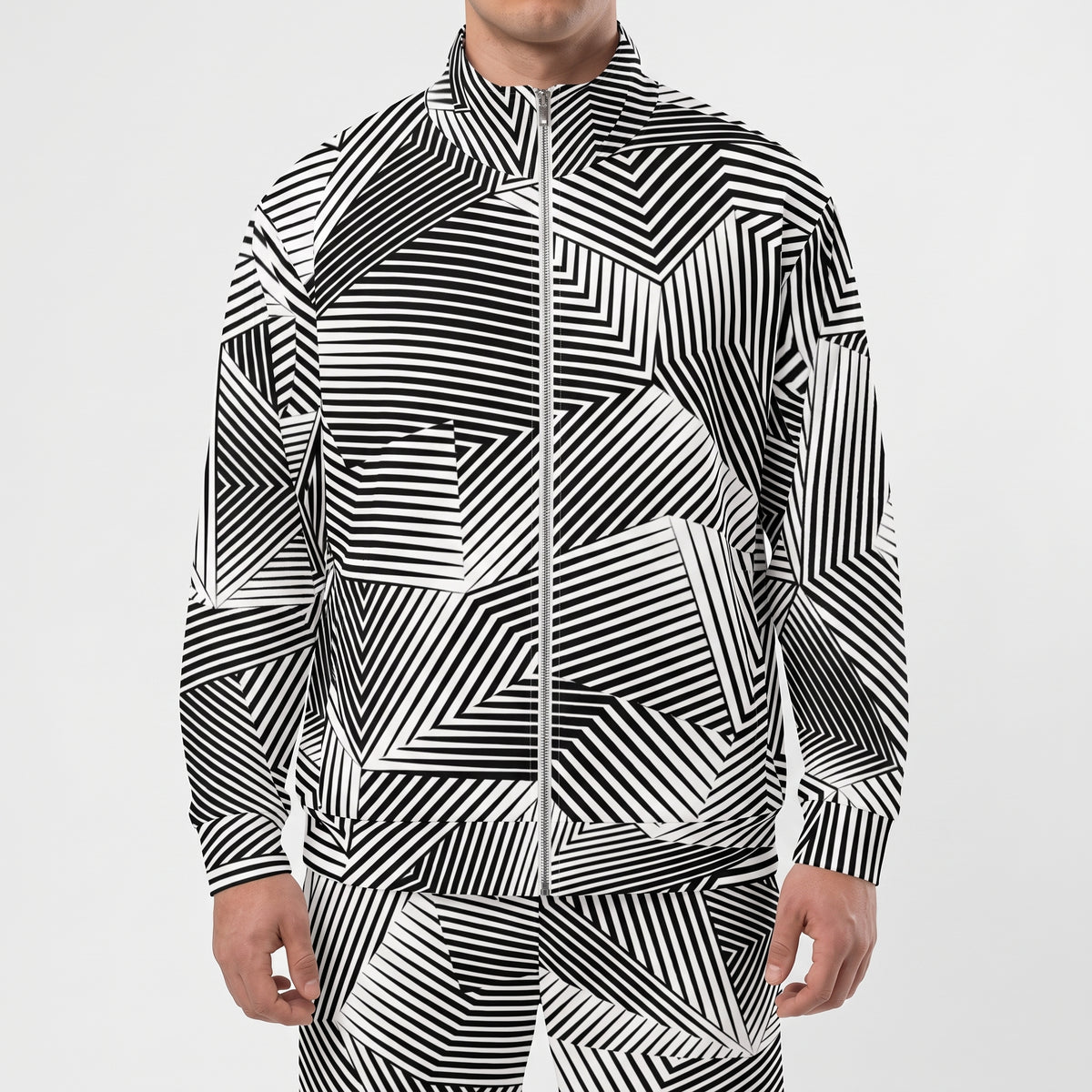 A man wearing a black and white geometric patterned zip-up jacket and matching pants against a light gray studio background.