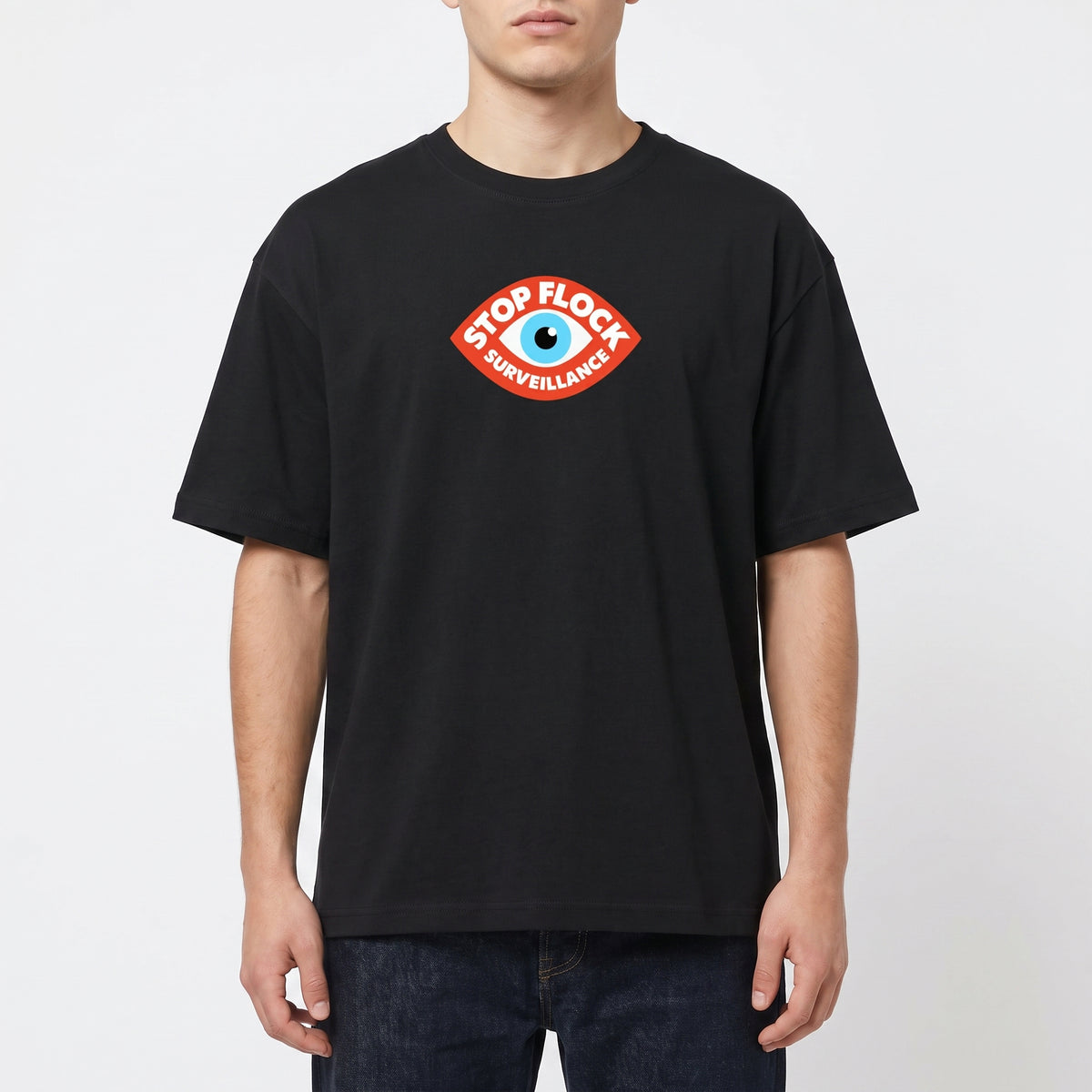 A man wearing a black crew-neck t-shirt with a red and blue 'Stop Flock Surveillance' eye graphic on the chest, paired with dark blue jeans, against a light gray background.
