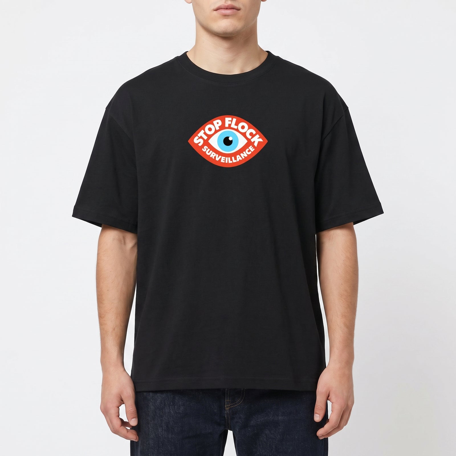 A man wearing a black crew-neck t-shirt with a red and blue 'Stop Flock Surveillance' eye graphic on the chest, paired with dark blue jeans, against a light gray background.
