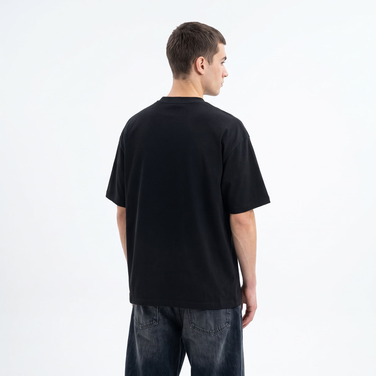 A man viewed from the back wearing a plain black short-sleeve t-shirt and dark blue jeans, standing against a clean white studio background.