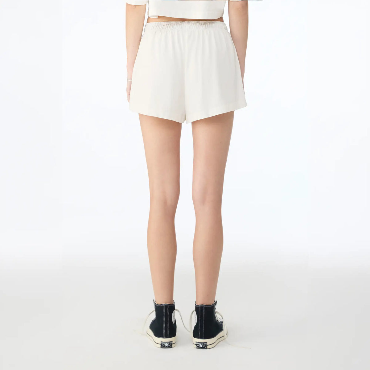 A model shown from the back wearing off-white shorts, a matching crop top, and black high-top sneakers against a plain white studio background.