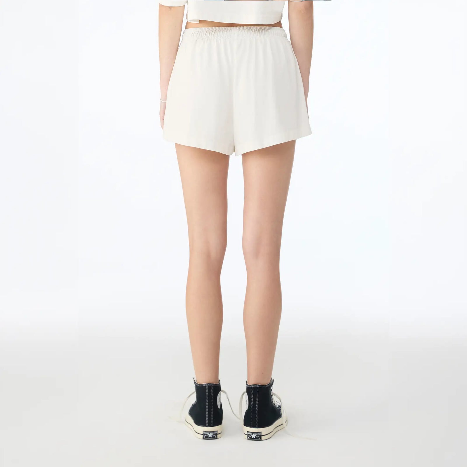 A model shown from the back wearing off-white shorts, a matching crop top, and black high-top sneakers against a plain white studio background.