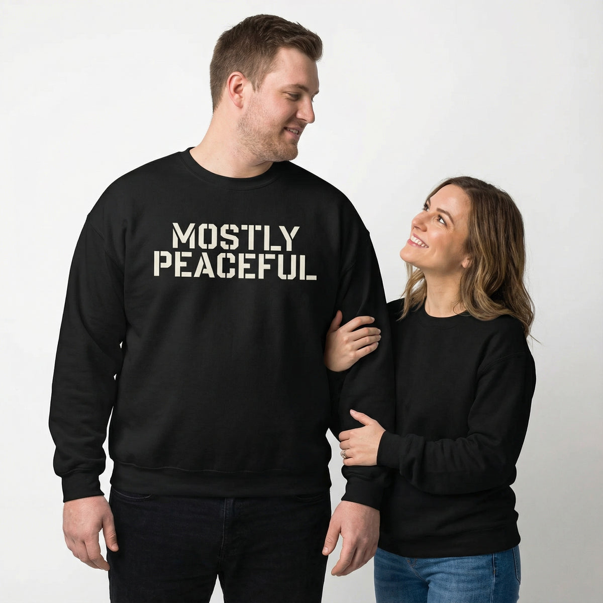 Two people wearing black sweatshirts with &#39;MOSTLY PEACEFUL&#39; text on a plain background