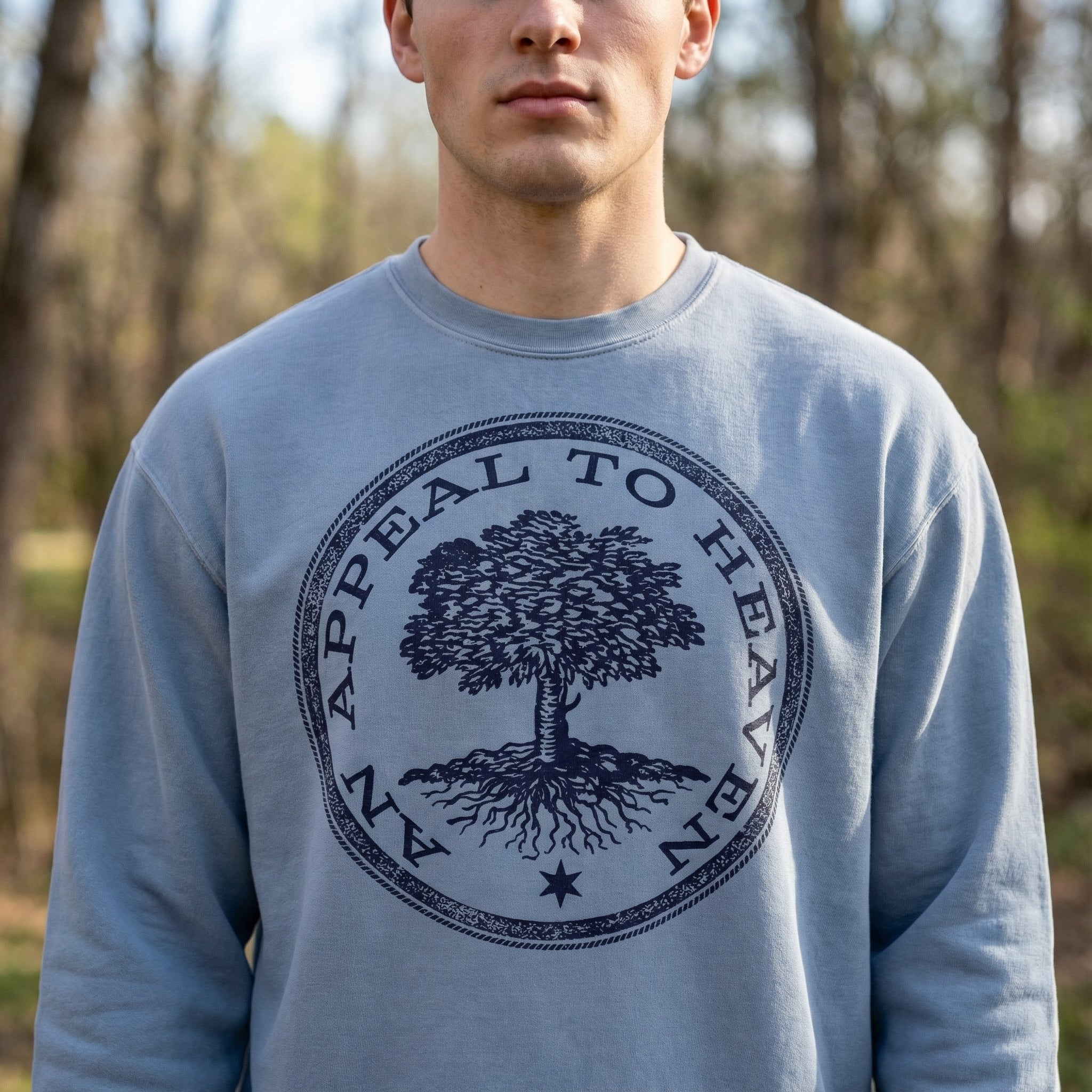 Person wearing a blue sweatshirt with a tree design and 'Appeal to Heaven' text in a forest setting
