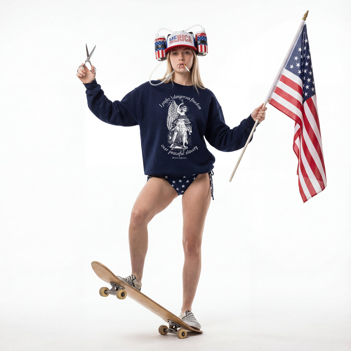 Person wearing a navy sweatshirt with an angel graphic, holding an American flag and a pair of scissors, standing on a skateboard.