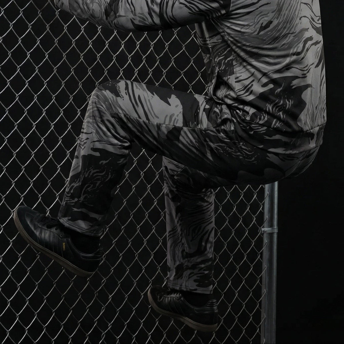 Person in tactical gear climbing a chain-link fence against a dark background