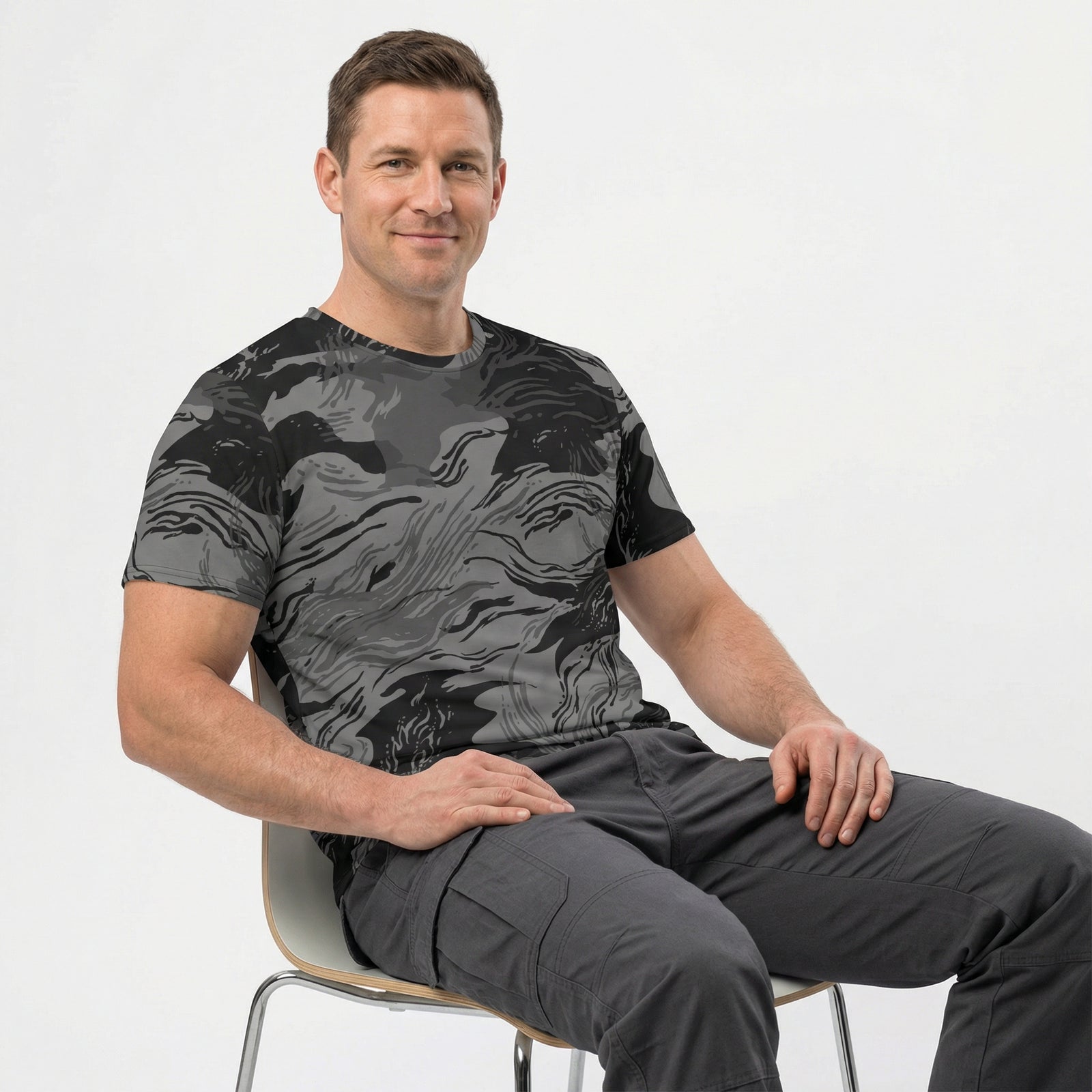 Man wearing a black and gray patterned shirt and pants sitting on a chair against a white background