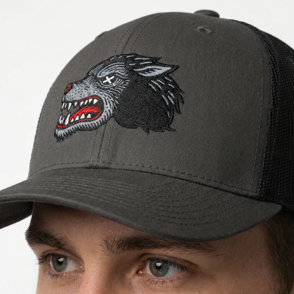 Gray cap with a wolf embroidered design worn by a person on a white background