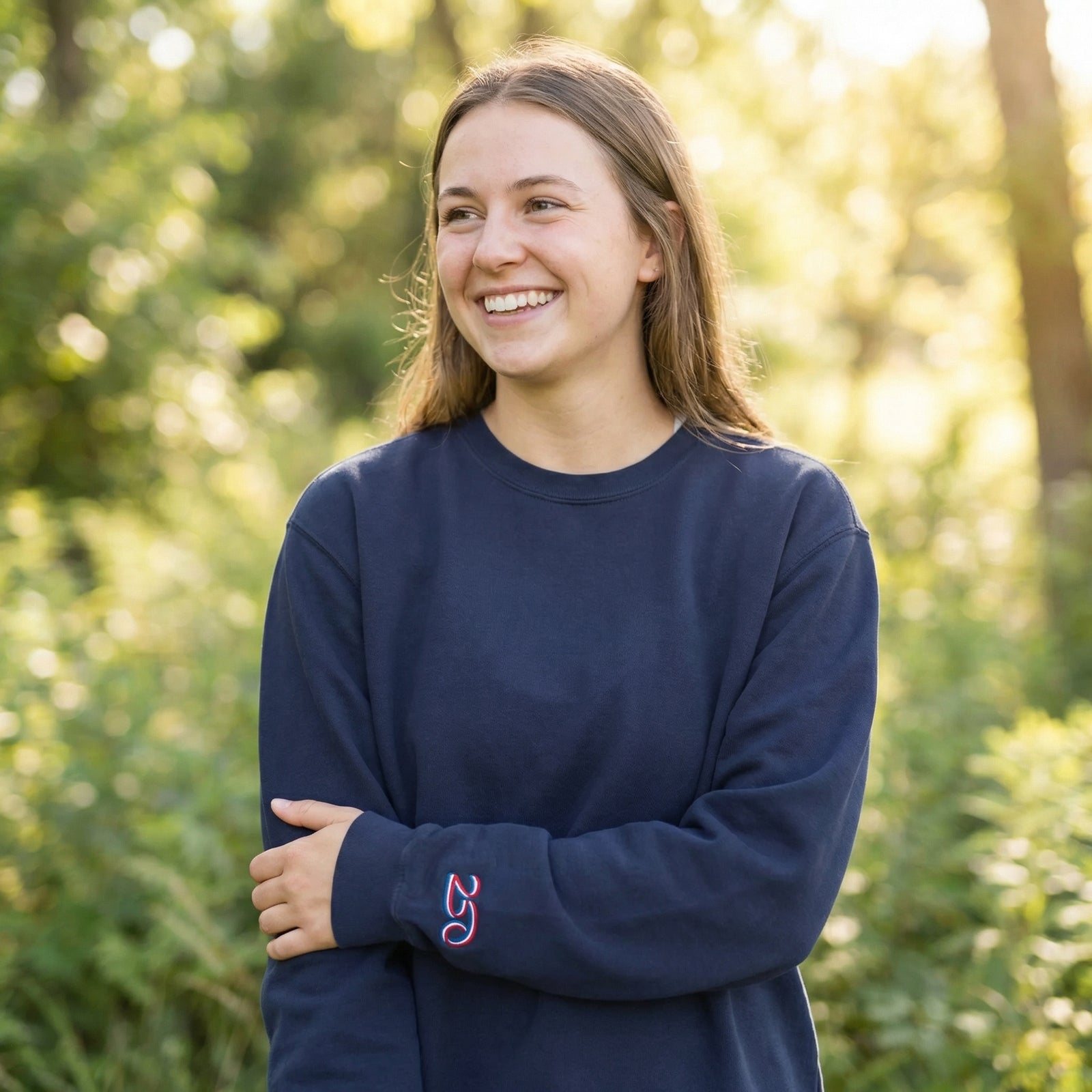 Woman wearing a navy blue sweatshirt with a logo, standing outdoors with greenery in the background