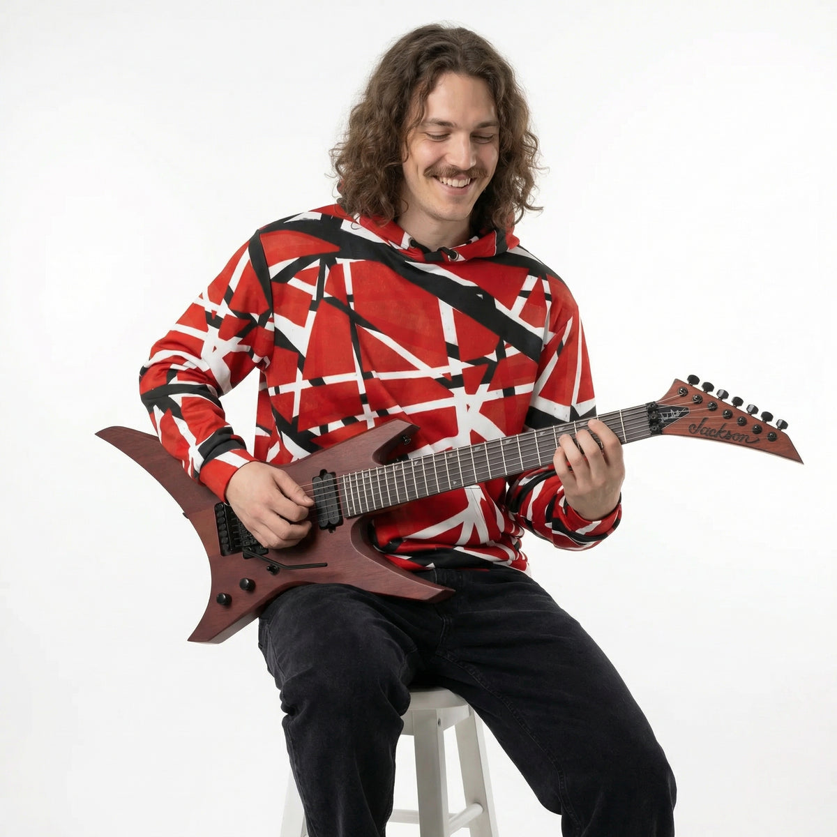A man wearing a red and black striped Frankenstripes Cotton Hoodie playing a 7 string Jackson Warrior electric guitar on a white background