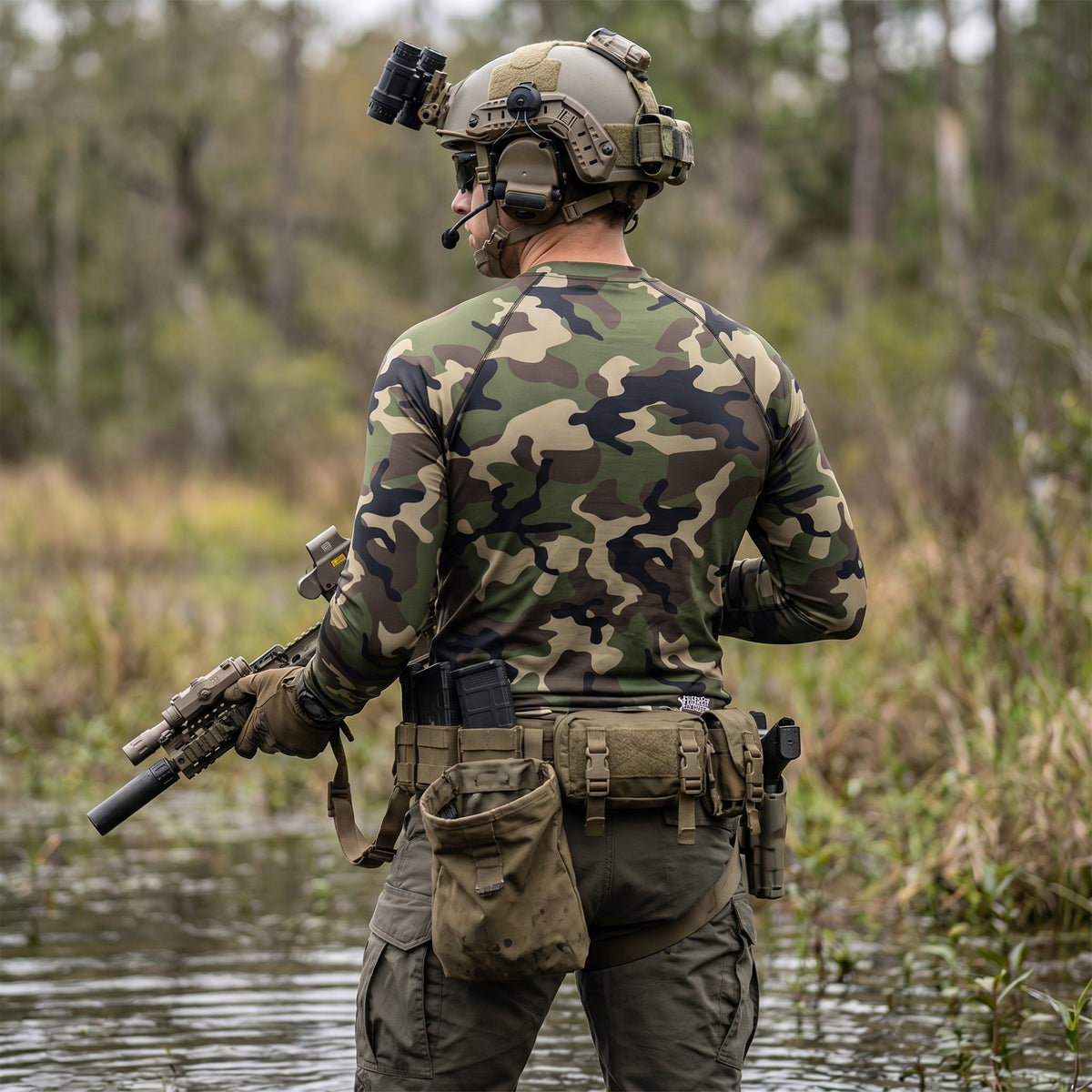 Person in camouflage gear with tactical equipment in a natural setting
