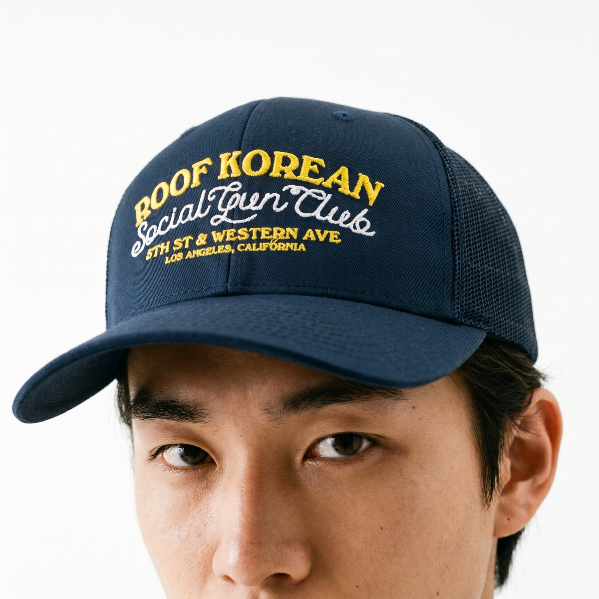 Navy blue cap with yellow and white text worn by a person on a white background