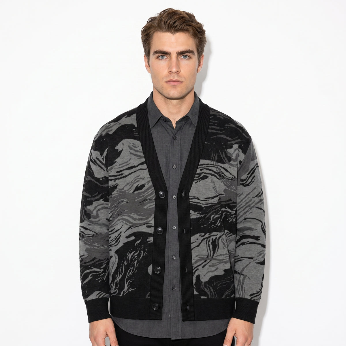 Man wearing a black and gray patterned cardigan over a gray shirt on a white background