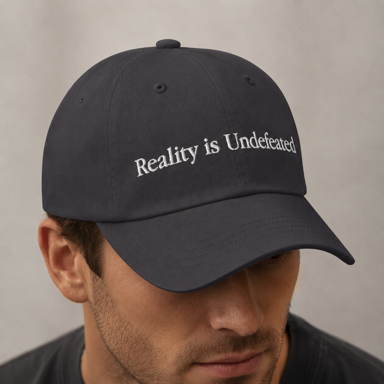 Man wearing a black cap with 'Reality is Undefeated' text on a neutral background