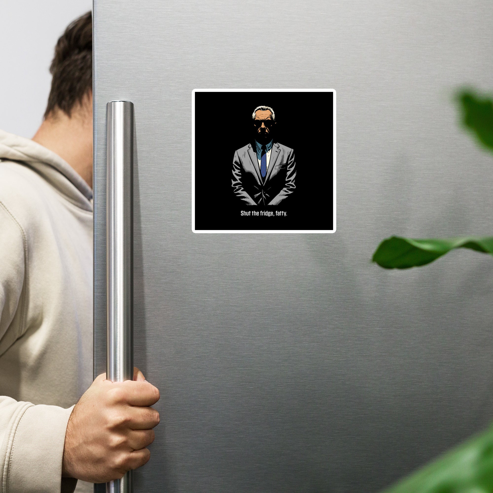 Person opening a refrigerator with a magnet featuring a man in a suit and text on the door.
