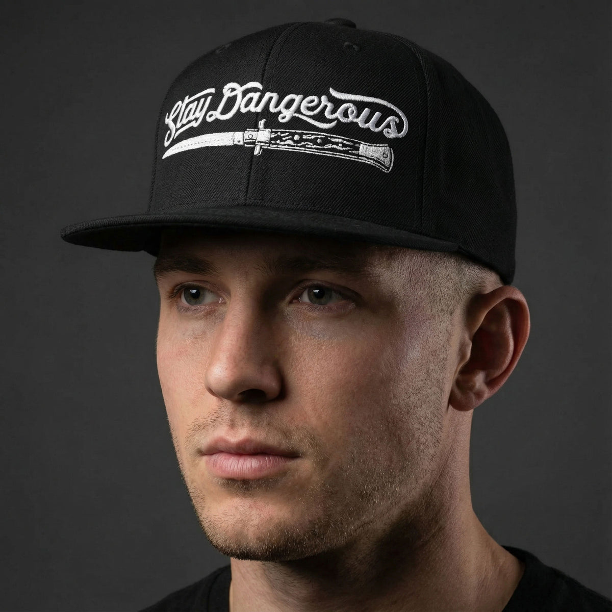 Man wearing a black cap with &#39;Stay Dangerous&#39; text on a dark background