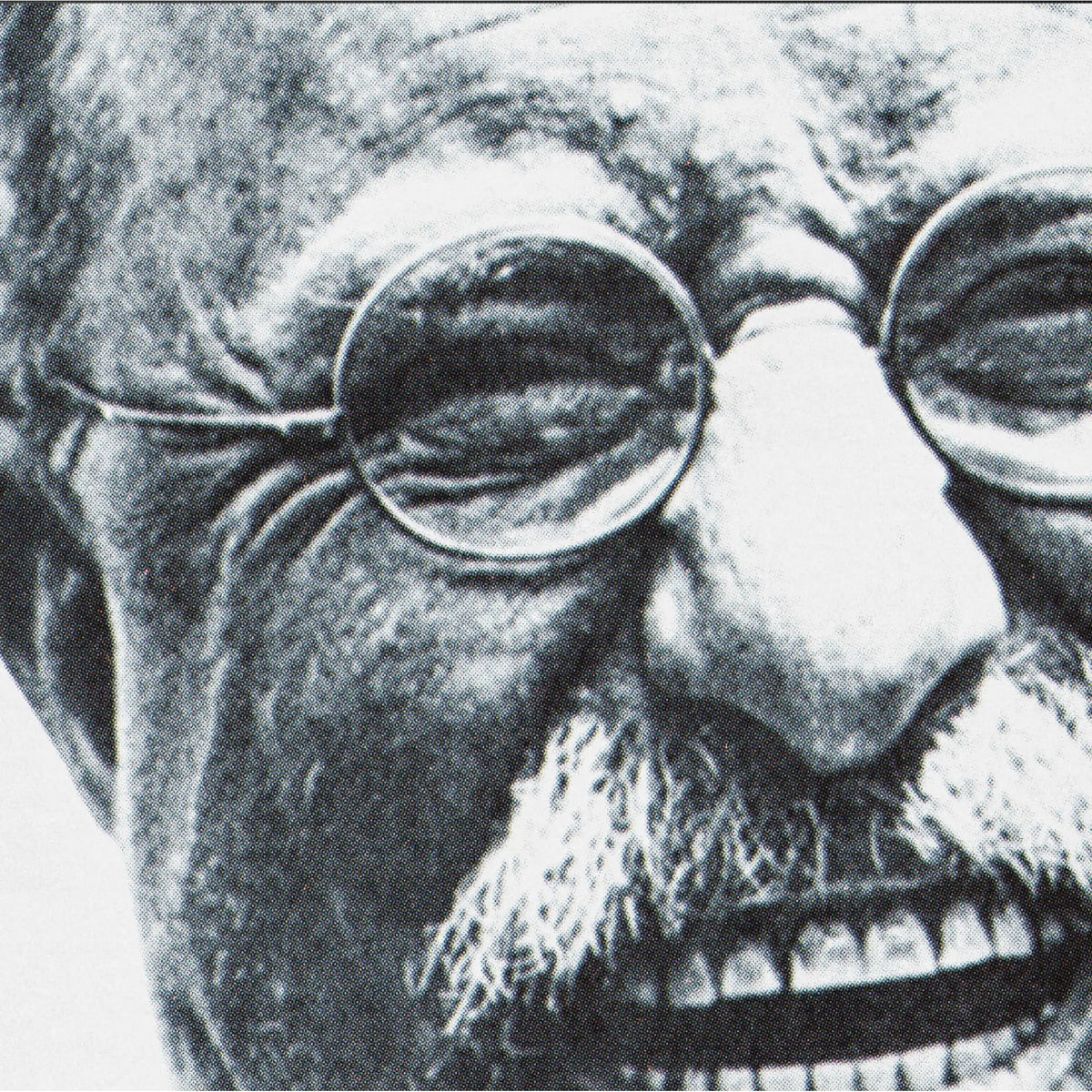Black and white close-up portrait of an Teddy Roosevelt wearing round wire-frame eyeglasses, with a mustache and wrinkled facial features.