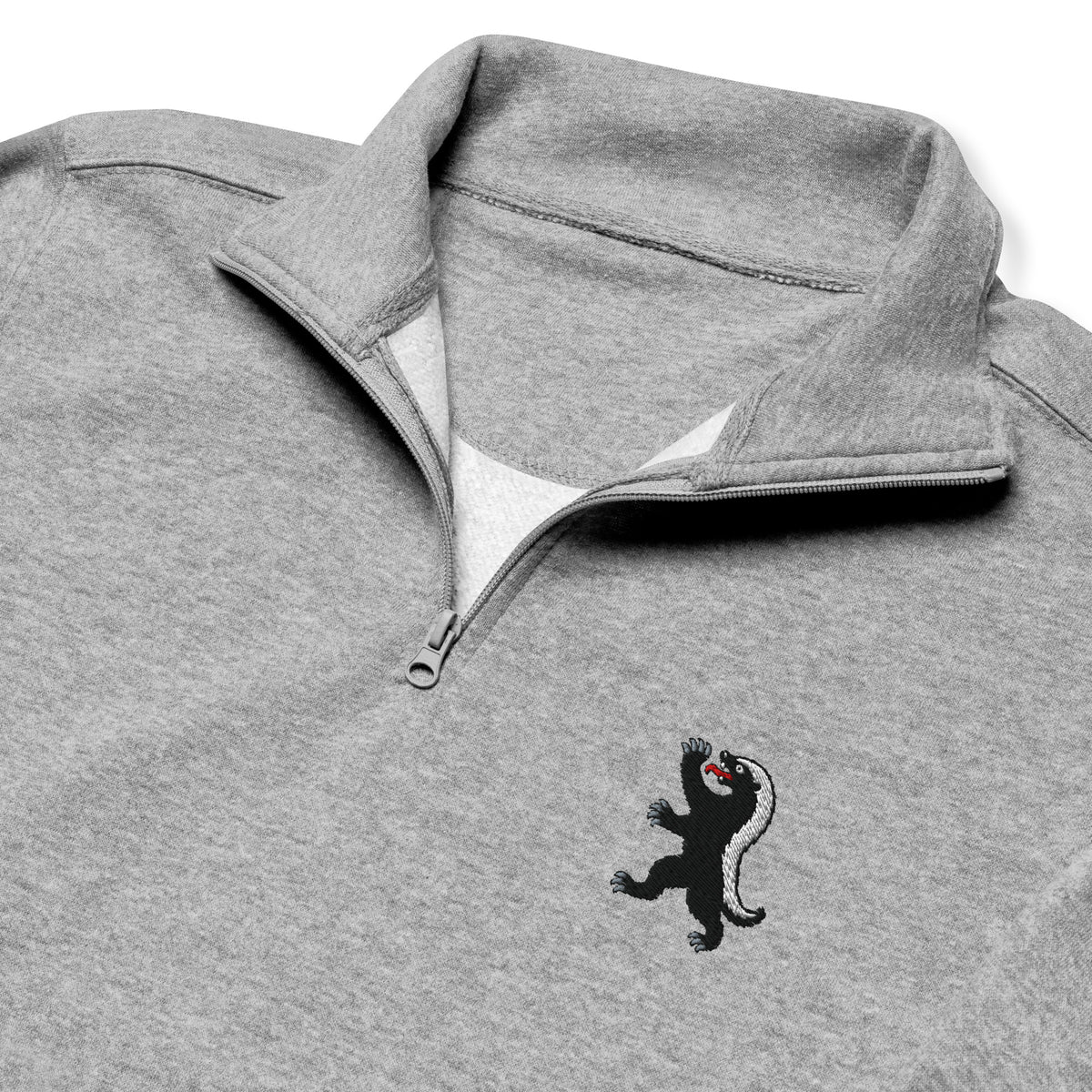 Close-up of the Carbon Grey honey badger quarter-zip, showing embroidered chest emblem, matching zipper, and soft fleece inside the collar