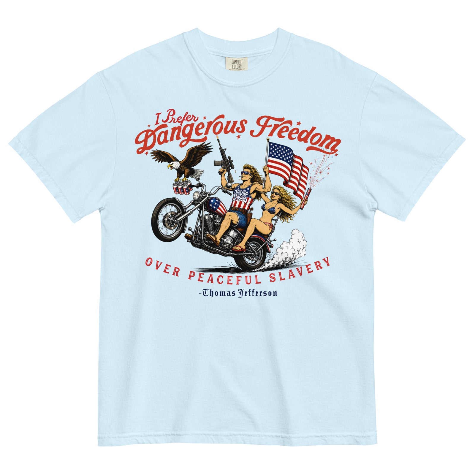 A light blue short-sleeve t-shirt featuring a retro-style illustration of a man and women on a motorcycle with American flags, an eagle, and fireworks. Red text above reads 'I Prefer Dangerous Freedom' and text below reads 'OVER PEACEFUL SLAVERY -Thomas Jefferson'. By Liberty Maniacs