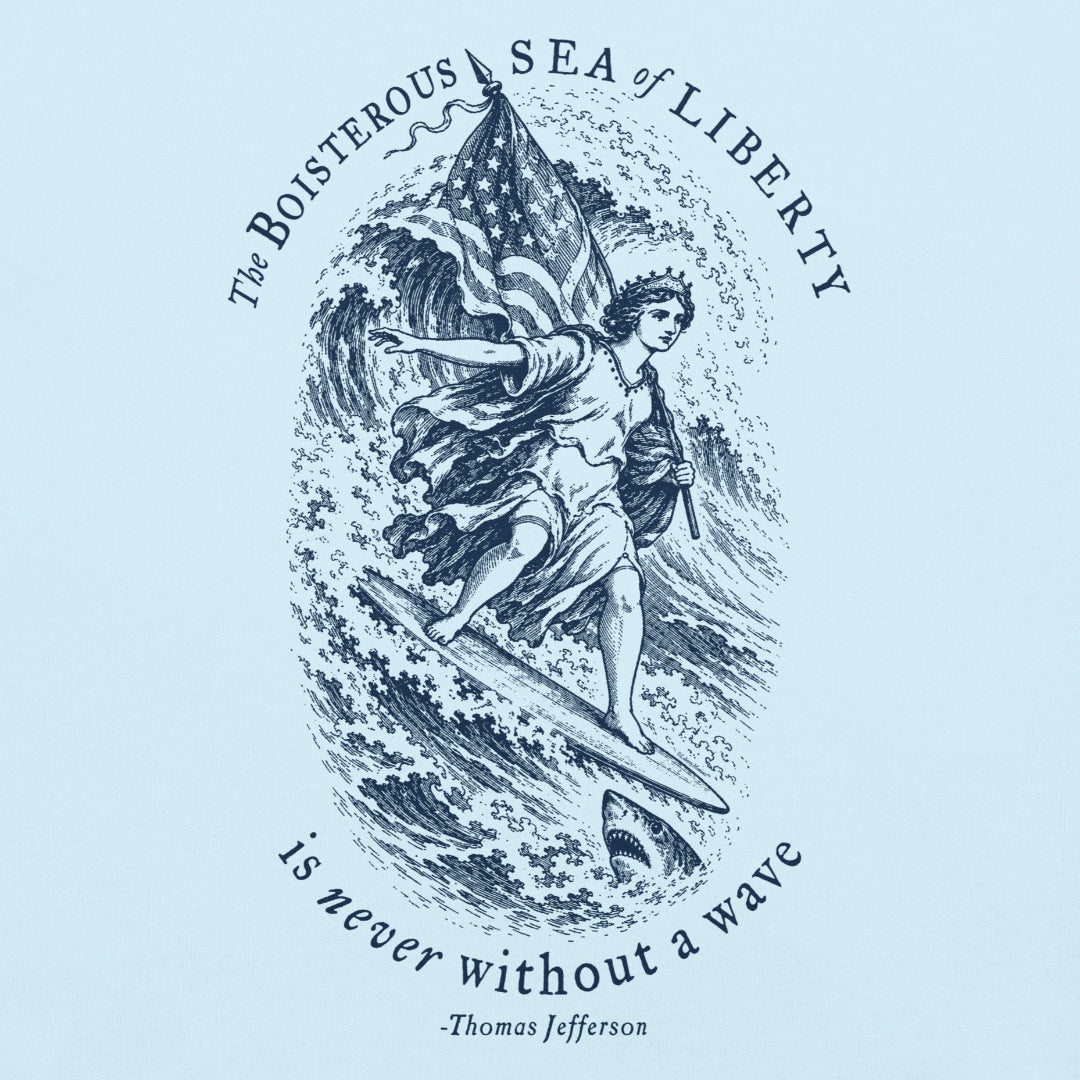 Close-up of navy Sea of Liberty print on Chambray fabric, showing surfing Liberty, American flag, shark and Jefferson quote