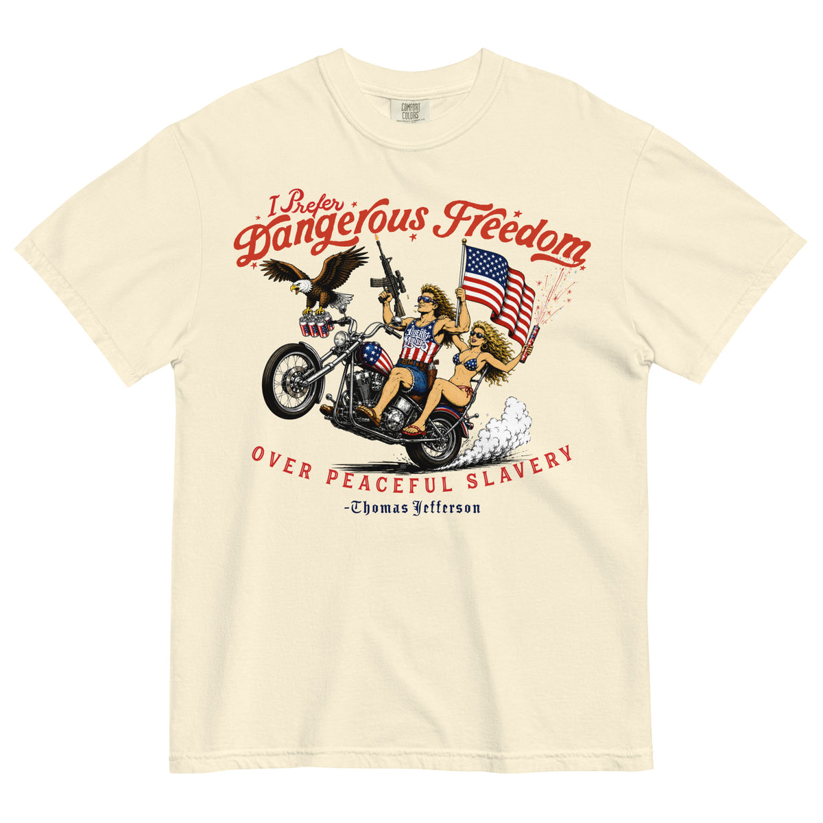 A cream-colored short-sleeve t-shirt featuring a retro-style illustration of a man and women on a motorcycle with American flags, an eagle, and fireworks. Red text above reads 'I Prefer Dangerous Freedom' and text below reads 'OVER PEACEFUL SLAVERY -Thomas Jefferson'. By Liberty Maniacs