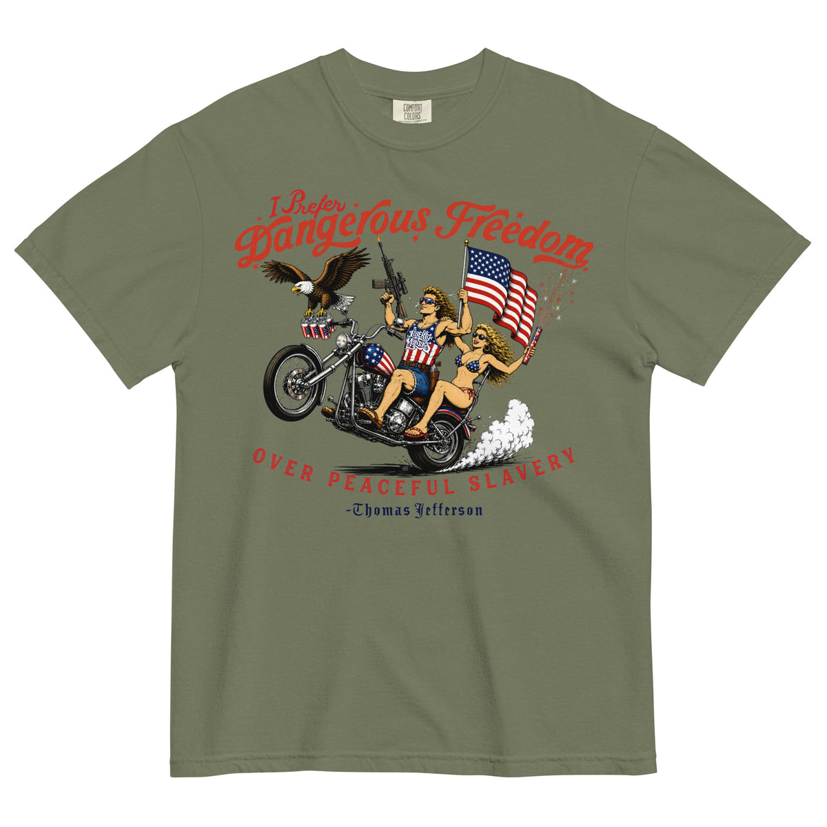 An olive green short-sleeve t-shirt featuring a retro-style illustration of a man and women on a motorcycle with American flags, an eagle, and fireworks. Red text above reads 'I Prefer Dangerous Freedom' and text below reads 'OVER PEACEFUL SLAVERY -Thomas Jefferson'. By Liberty Maniacs