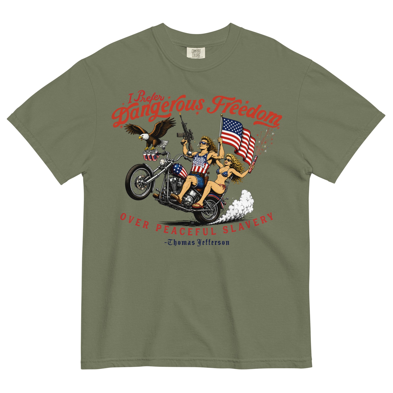 An olive green short-sleeve t-shirt featuring a retro-style illustration of a man and women on a motorcycle with American flags, an eagle, and fireworks. Red text above reads 'I Prefer Dangerous Freedom' and text below reads 'OVER PEACEFUL SLAVERY -Thomas Jefferson'. By Liberty Maniacs