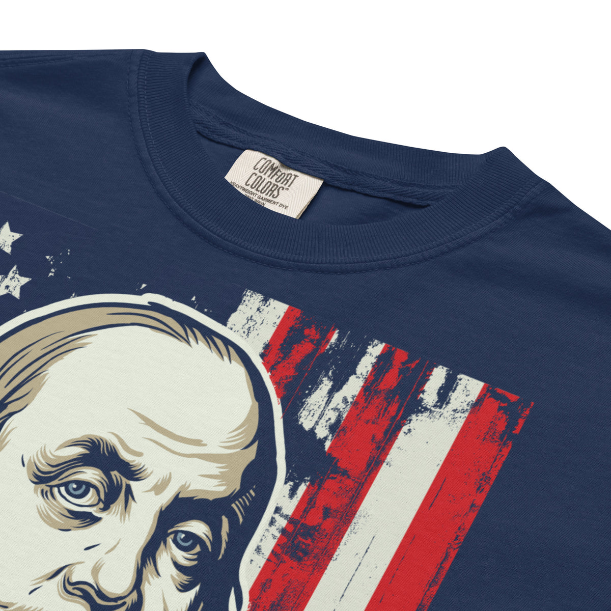 Close-up of a navy blue t-shirt featuring a graphic print of a man's face next to a distressed red, white, and blue American flag design. The inside collar shows a brand label for 'Combat Colors'.