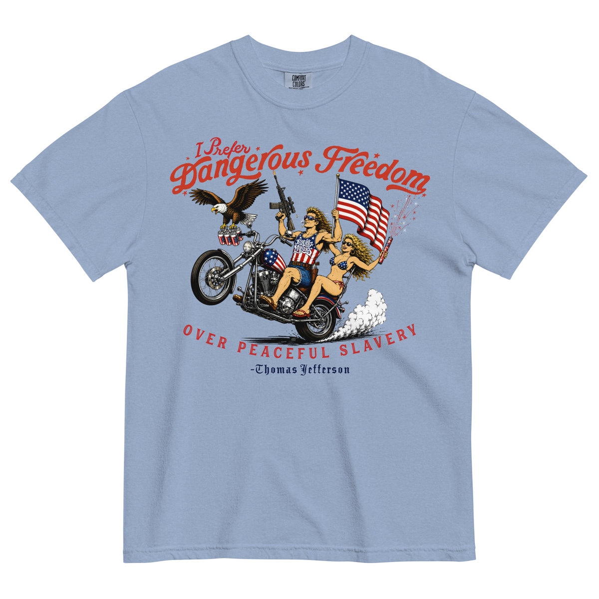 A light blue crewneck t-shirt featuring a retro-style illustration of a man and women on a motorcycle with American flags, an eagle, and fireworks. Red text above reads 'I Prefer Dangerous Freedom' and text below reads 'OVER PEACEFUL SLAVERY -Thomas Jefferson'. By Liberty Maniacs
