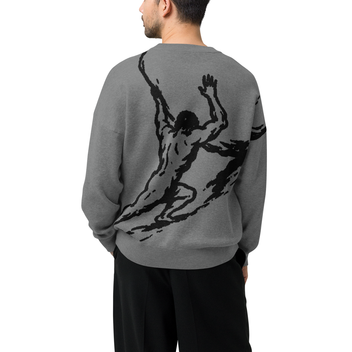 A man viewed from the back wearing a gray crewneck sweater with a large black abstract figure graphic on the back, paired with black pants and black shoes, against a plain white background.