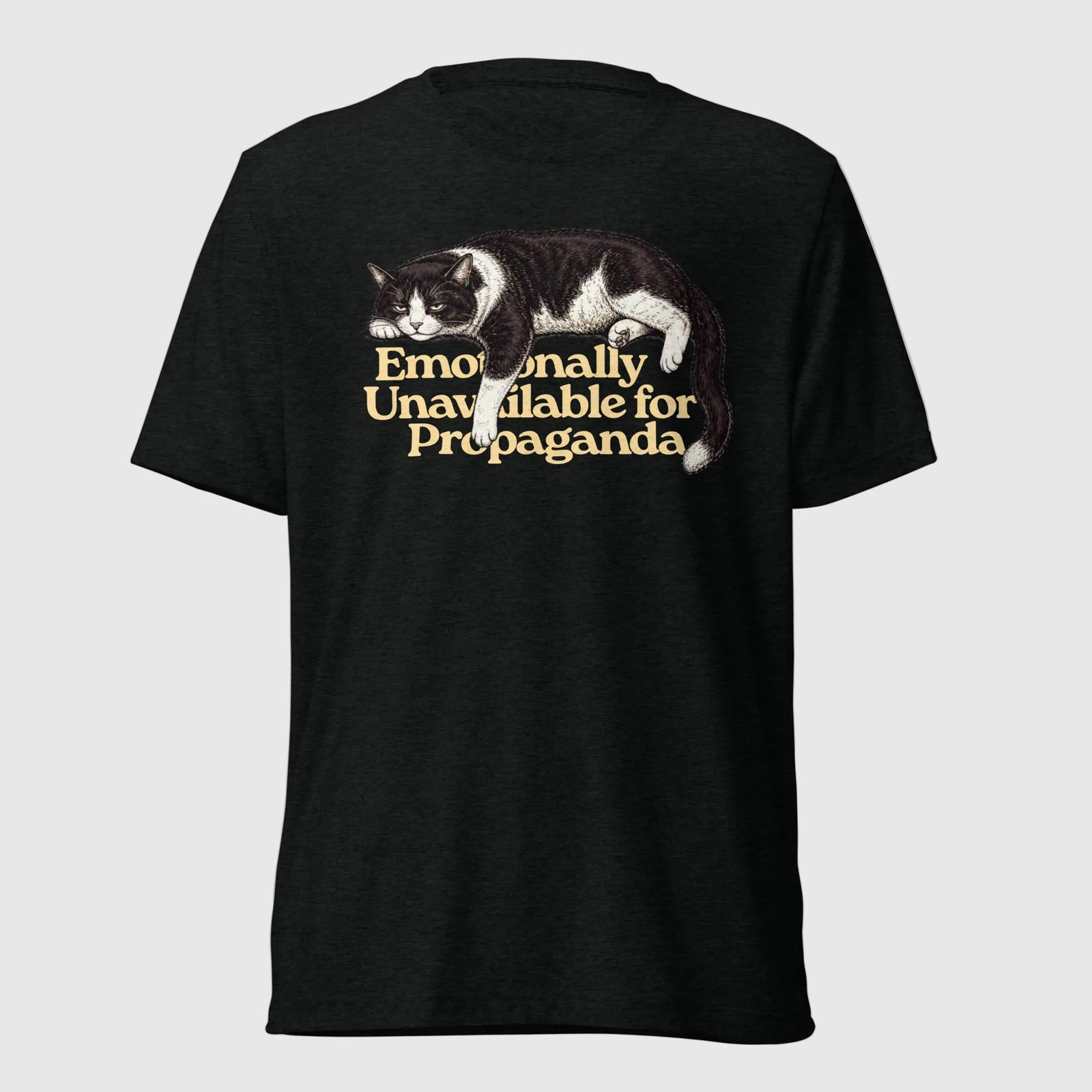 A black short-sleeve t-shirt with a graphic of a black and white cat lying down next to the text 'Emotionally Unavailable for Propaganda' in a gold serif font, shown against a plain white background.
