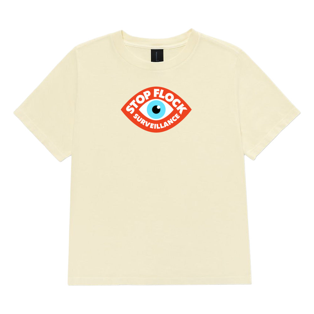 A cream-colored short-sleeve t-shirt with a red and blue 'Stop Flock Surveillance' eye graphic printed on the center chest, displayed against a plain white background.