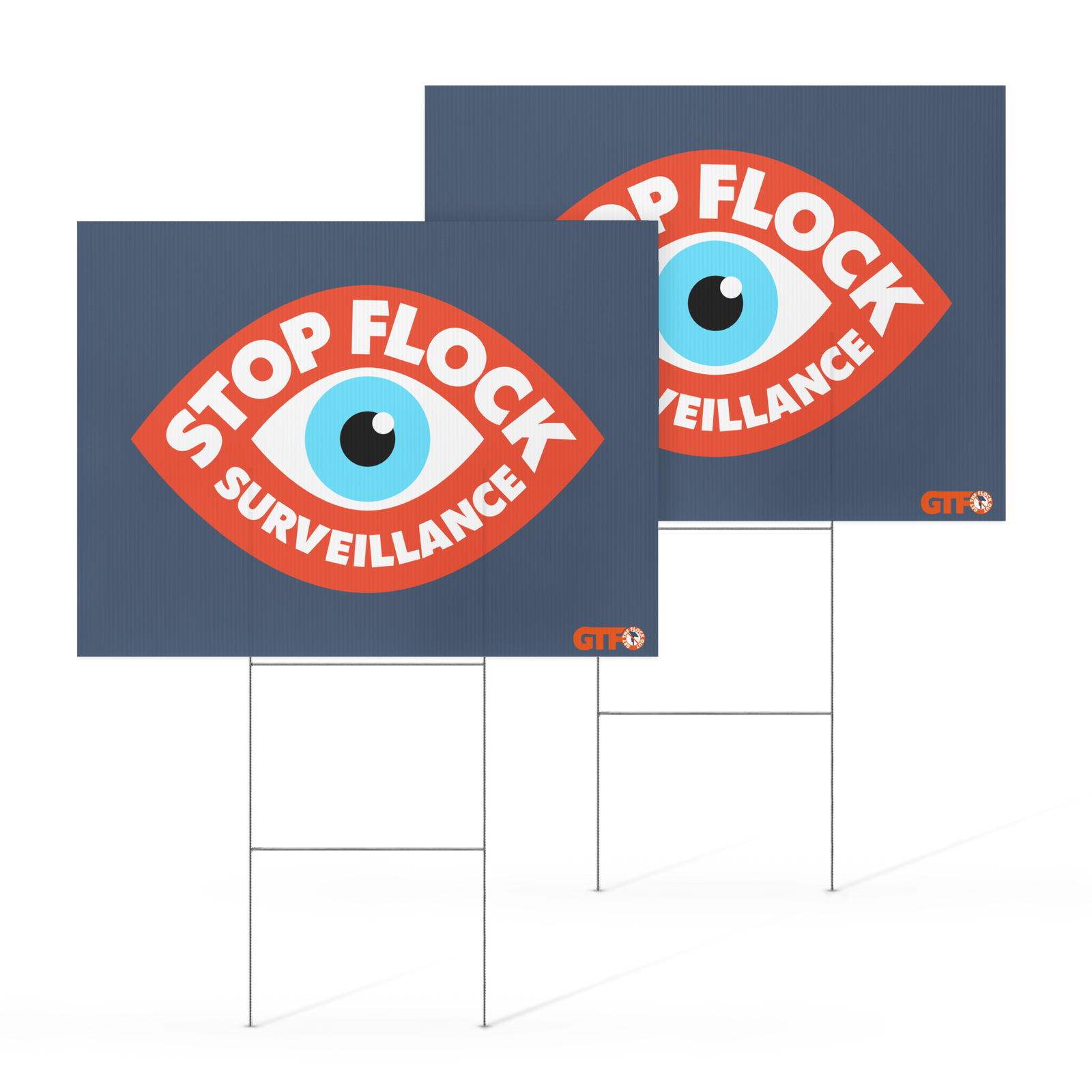 Two navy blue yard signs with metal wire stakes, featuring a red eye-shaped graphic with the words 'STOP FLOCK SURVEILLANCE' in white and a blue-and-white eye. A small orange 'OTC' logo appears near the bottom right of each sign.